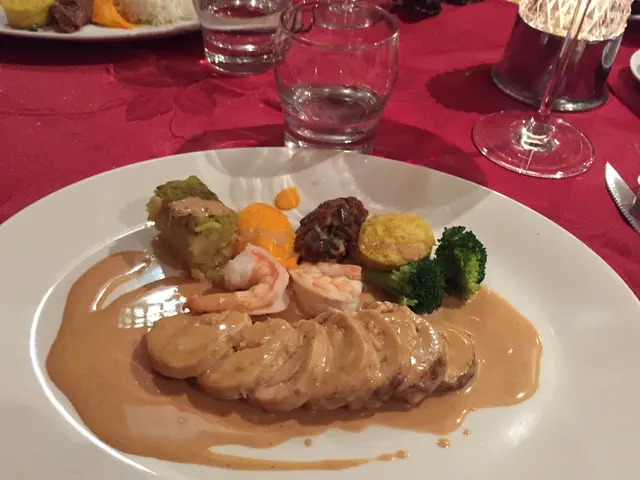 The picture consists of a table covered with red cloth. In the picture there are plates, glasses,...