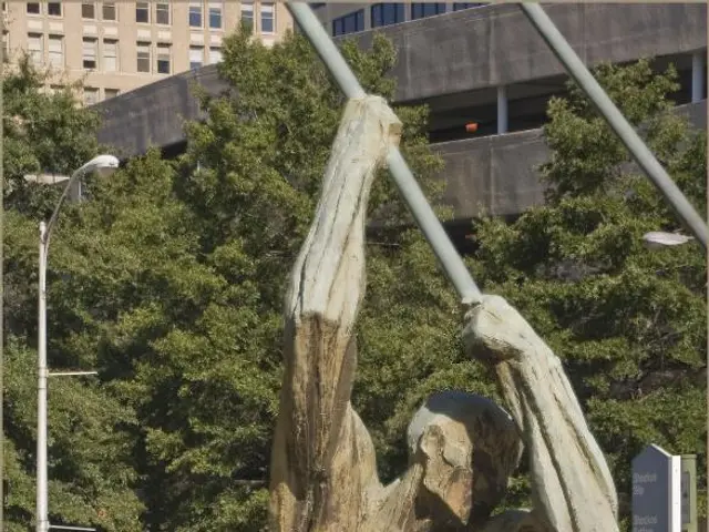 Here we can see a statue. Background there is a light pole, buildings, trees, signboards, stores...